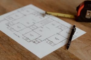 A floor plan on a wooden surface with a retractable tape measure and a mechanical pencil