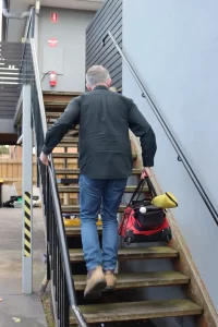 Building inspector carrying a toolkit up exterior stairs to inspect a property during a professional building inspection.