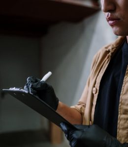 A man wearing safety vest writing on a clipboard placed on a wooden table