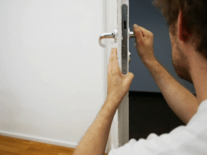 A man in a white shirt checking the door handles in a room.