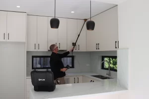 Professional pest control technician using equipment to inspect and treat high kitchen cabinets for pest prevention.