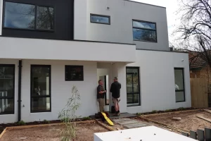 Pre-handover inspection of a newly built modern home with inspectors checking exterior finishes.