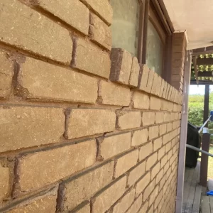 Close-up of cracked brickwork and mortar joints along an exterior house wall beneath a window.