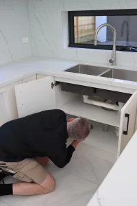Building inspector checking plumbing and moisture levels under kitchen sink during a Melbourne building inspection