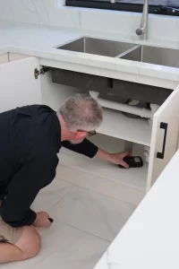 Building inspector using moisture meter under kitchen sink cabinet during Melbourne property inspection