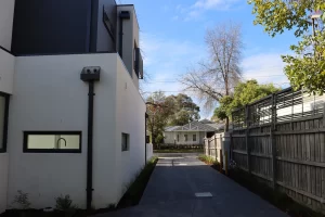 Modern house side driveway with narrow access between a rendered wall and timber boundary fence.