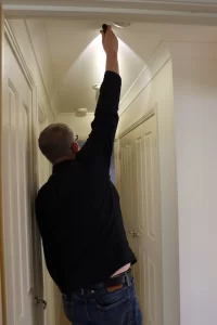 Inspector checking ceiling light fixture for defects and alignment inside residential property
