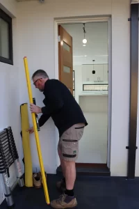 Builder inspecting door frame alignment with level during pre-handover inspection Melbourne